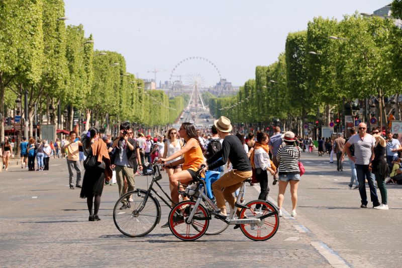 Fahrradfahrer zwischen Fußgängern in Paris auf einer Allee. Im Hintergrund das Riesenrad auf der Place de la Concorde.