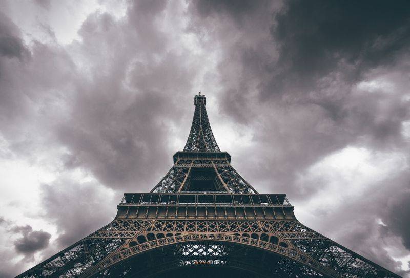 Klassenfahrt Paris Tickets Eiffelturm - auf dem Bild sehen wir den Eiffelturm in schwarz-weiß von unten mit seiner Spitze in einem bewölkten Himmel.